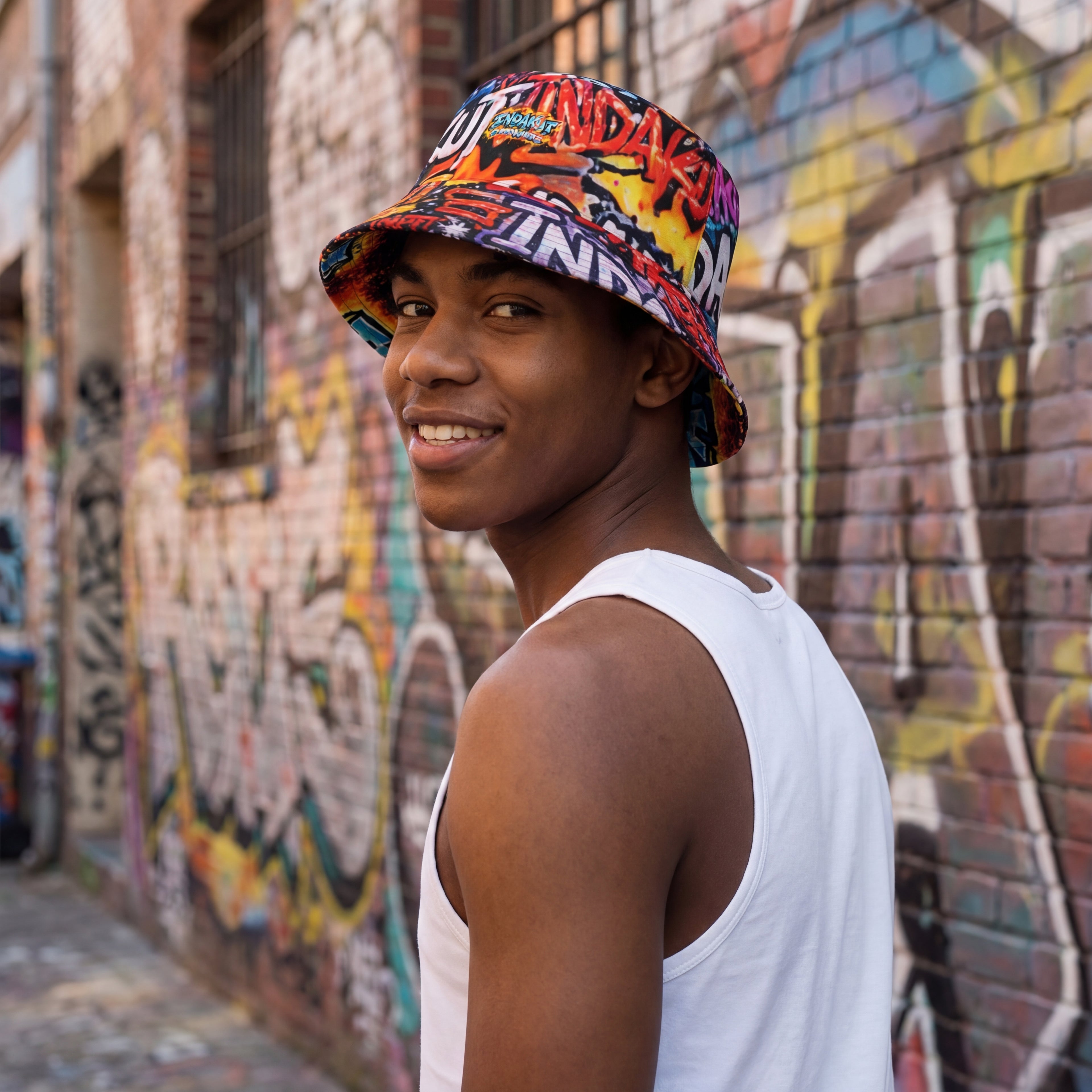 close-up of model wearing graffiti print reversible bucket hat against graffiti wall in urban setting